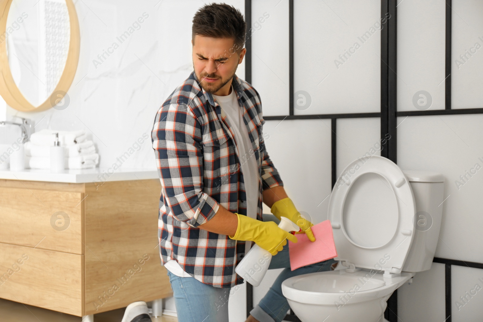 Photo of Young man feeling disgust while cleaning toilet bowl in bathroom