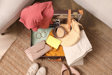 Photo of Open suitcase with different women clothes and accessories on carpet, top view