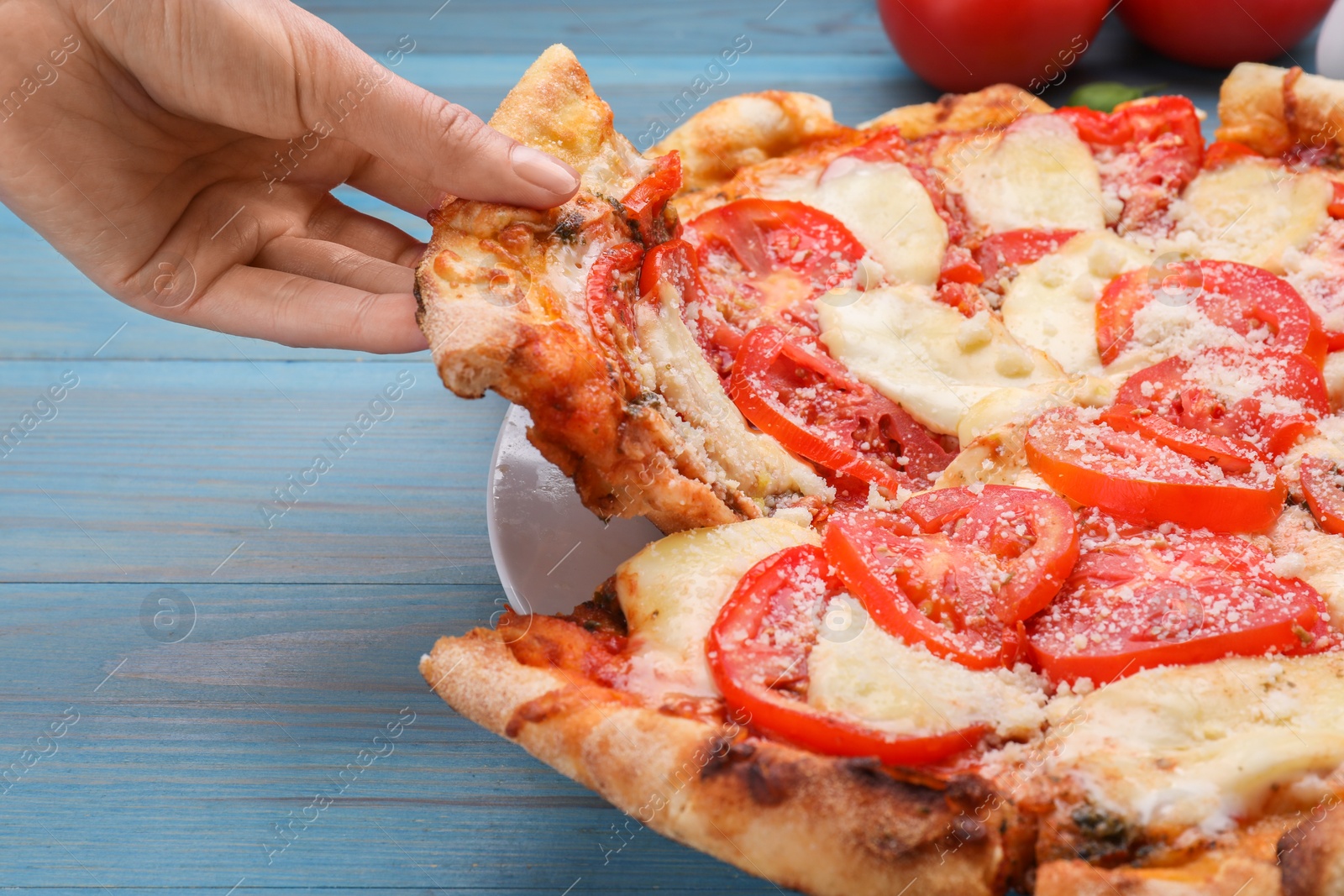 Photo of Woman taking piece of delicious Caprese pizza at blue wooden table, closeup