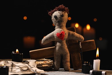 Photo of Voodoo doll with pin in heart and ceremonial items on wooden table against blurred background