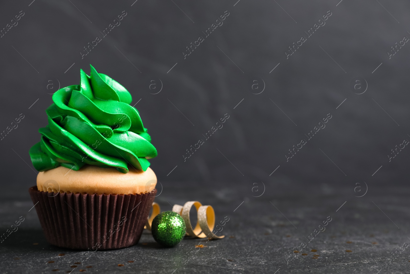 Photo of Delicious cupcake with green cream and Christmas decor on black table. Space for text