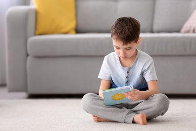 Photo of Cute little boy with book sitting on floor at home