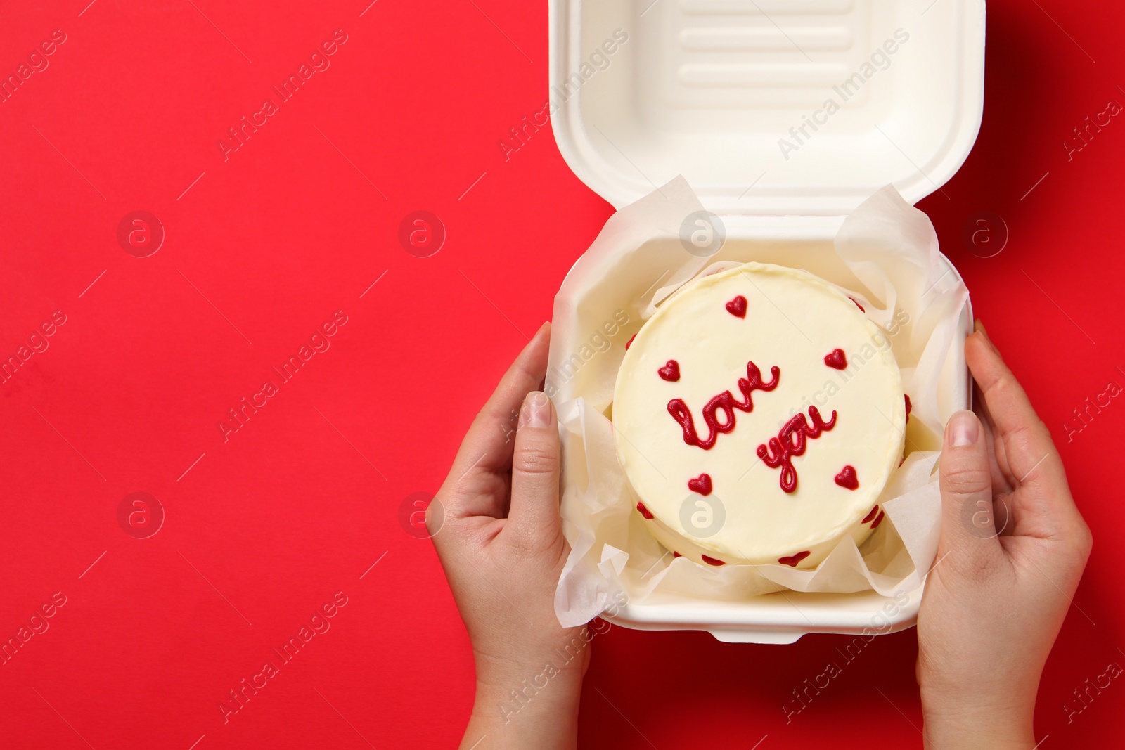 Photo of Woman holding takeaway box with bento cake at red table, closeup. St. Valentine's day surprise