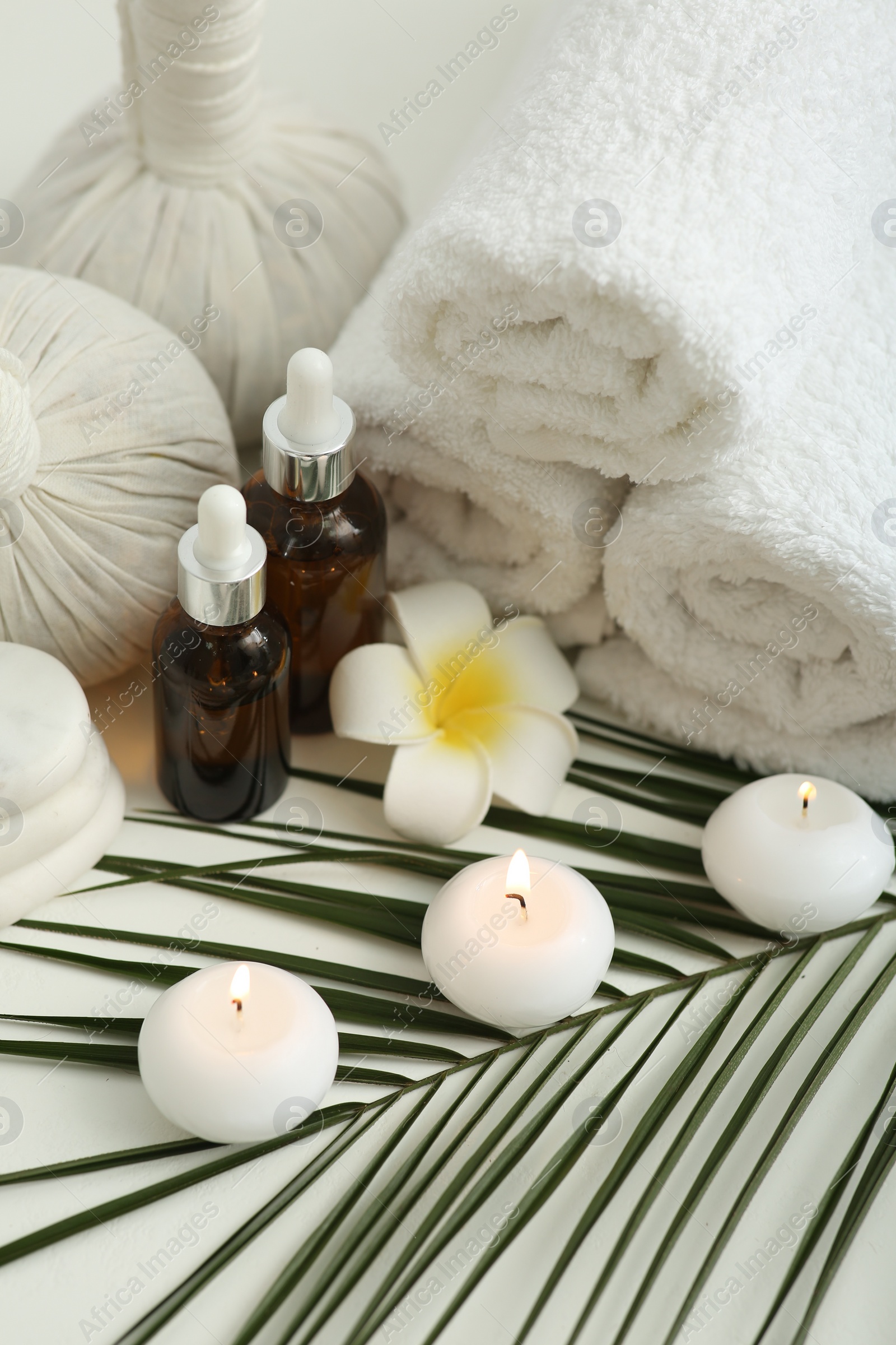 Photo of Composition with different spa products, burning candles and plumeria flower on white table