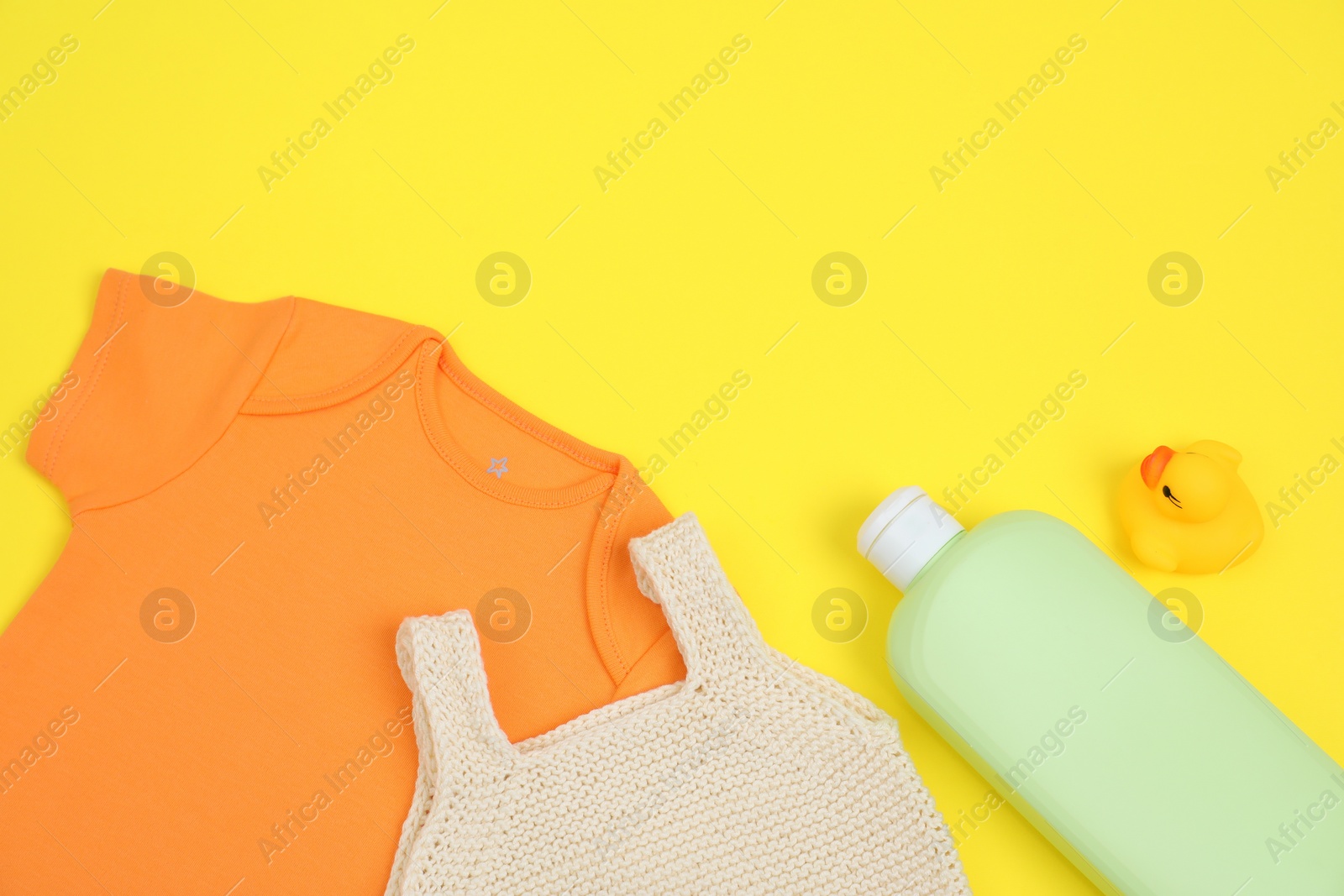 Photo of Bottles of laundry detergents, baby clothes and rubber duck on yellow background, flat lay. Space for text