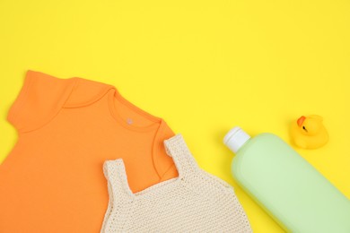 Bottles of laundry detergents, baby clothes and rubber duck on yellow background, flat lay. Space for text