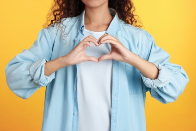Photo of African-American woman making heart with hands on yellow background, closeup