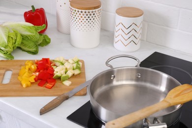 Photo of Wooden board with cut vegetables and knife near saute pan in kitchen