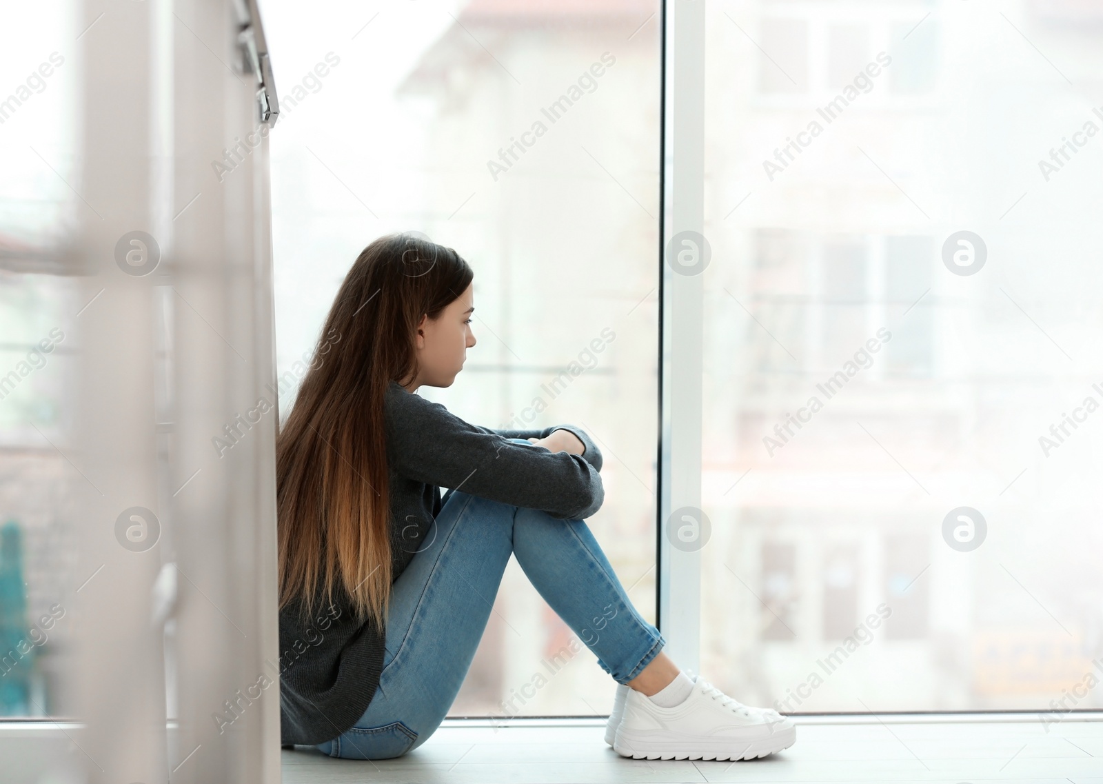 Photo of Upset teenage girl sitting at window indoors. Space for text