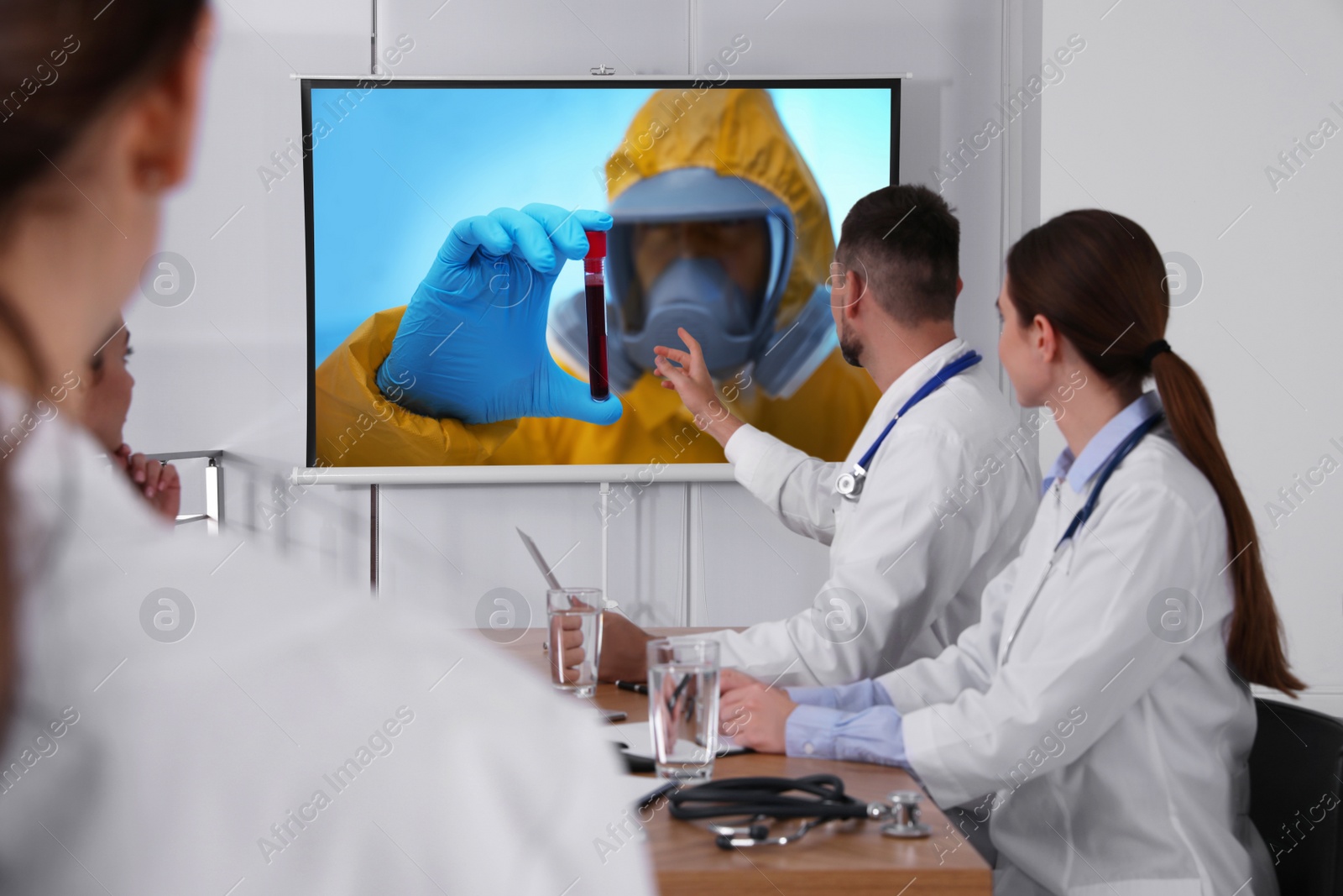 Image of Team of doctors using video projector during coronavirus conference in office