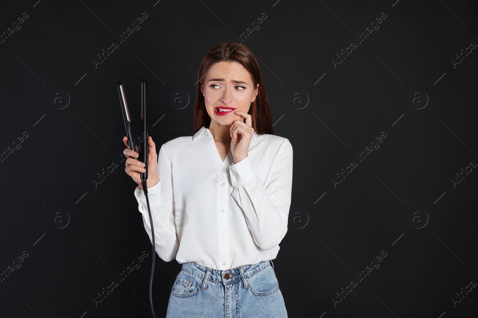 Photo of Upset young woman with flattening iron on black background. Hair damage