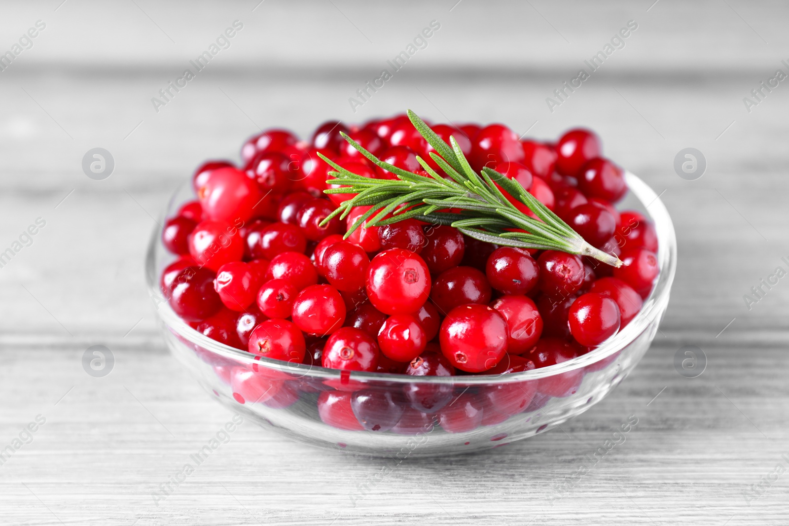 Photo of Fresh ripe cranberries and rosemary in bowl on grey wooden table, closeup