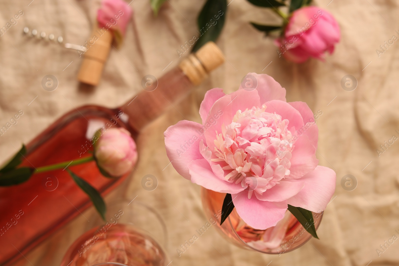 Photo of Beautiful pink peony in glass of rose wine on beige fabric, top view