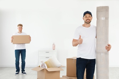 Photo of Moving service employees with cardboard boxes and carpet in room