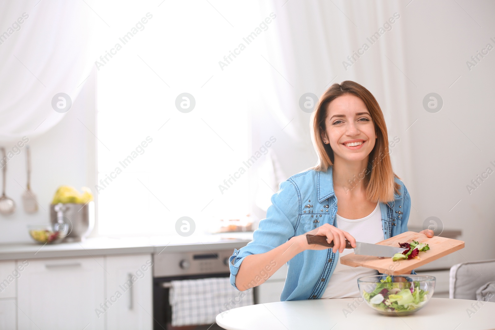 Photo of Happy young woman preparing salad in kitchen, space for text. Healthy diet