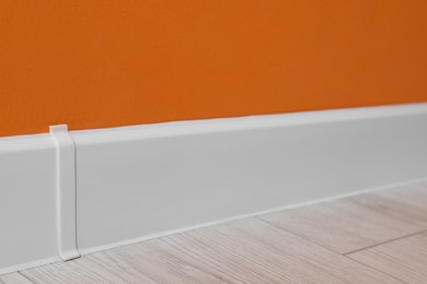 White plinth on laminated floor near orange wall indoors, closeup
