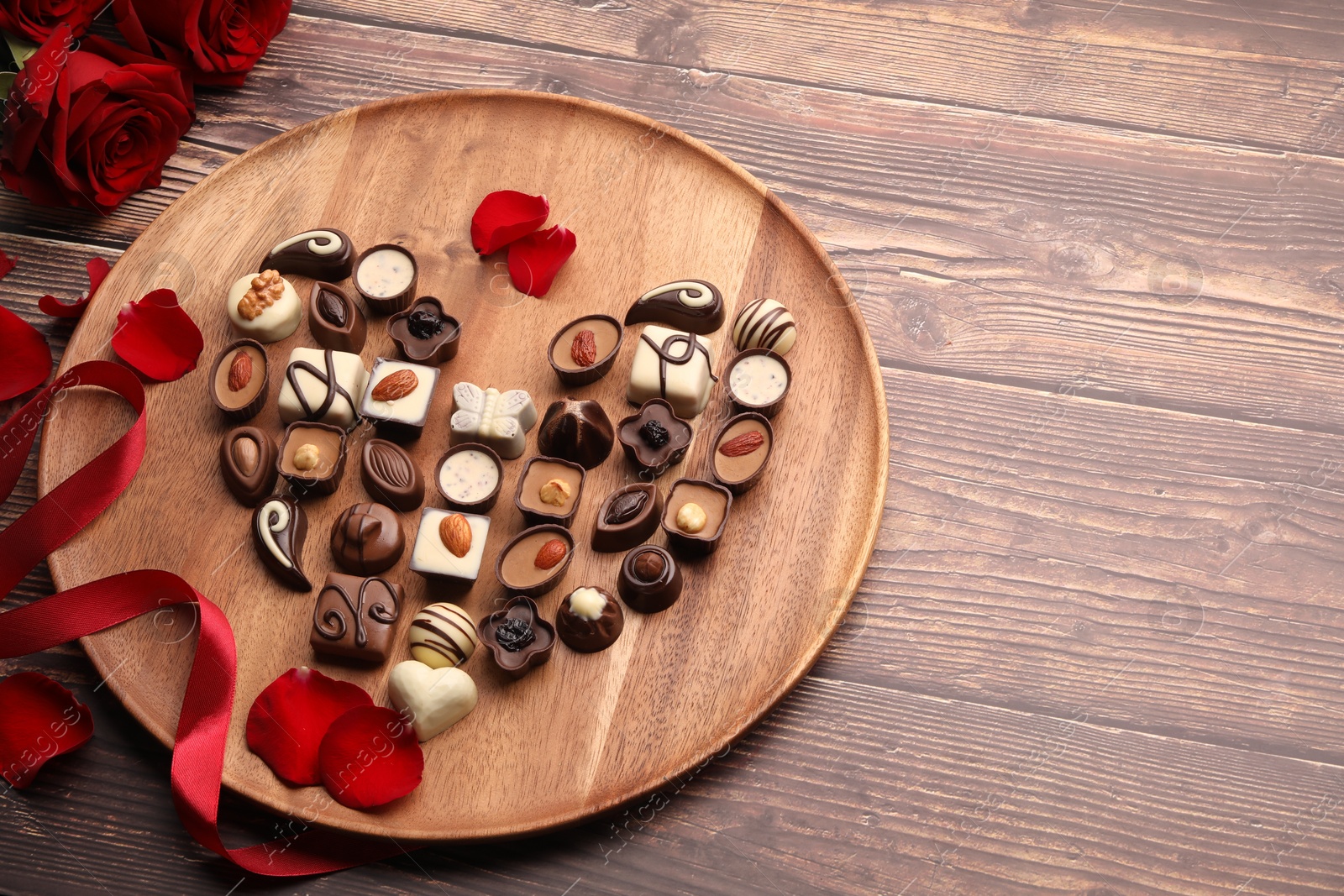 Photo of Heart made with delicious chocolate candies and rose petals on wooden table. Space for text