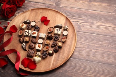 Photo of Heart made with delicious chocolate candies and rose petals on wooden table. Space for text