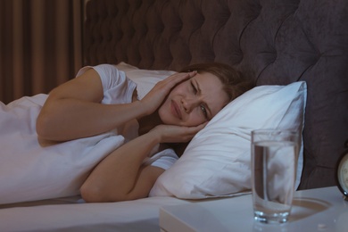 Photo of Young woman with terrible headache lying in bed at night