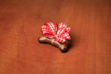 Photo of Bone shaped dog cookie with red bow on wooden background