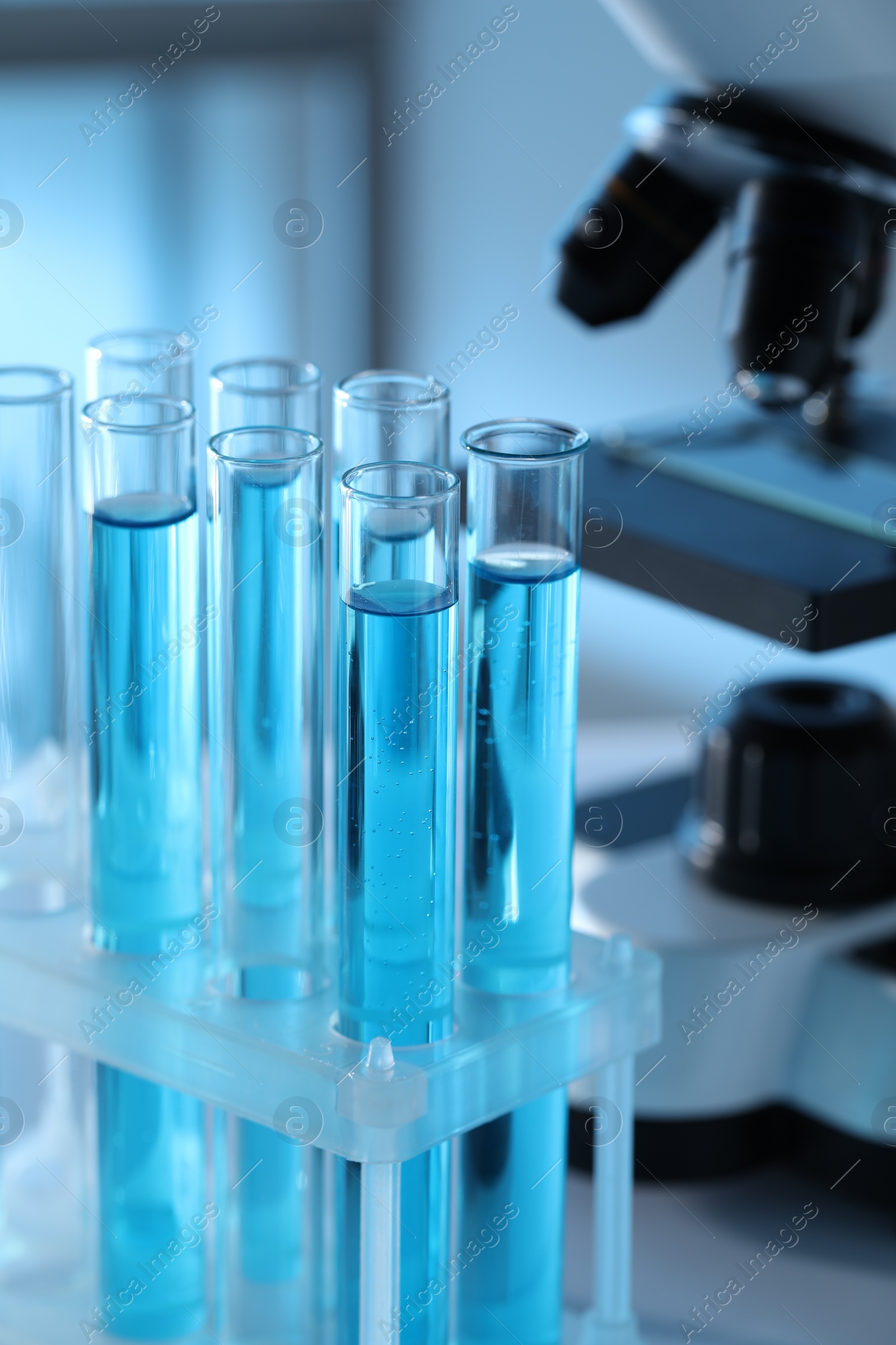 Photo of Test tubes with light blue liquid near microscope in laboratory, closeup