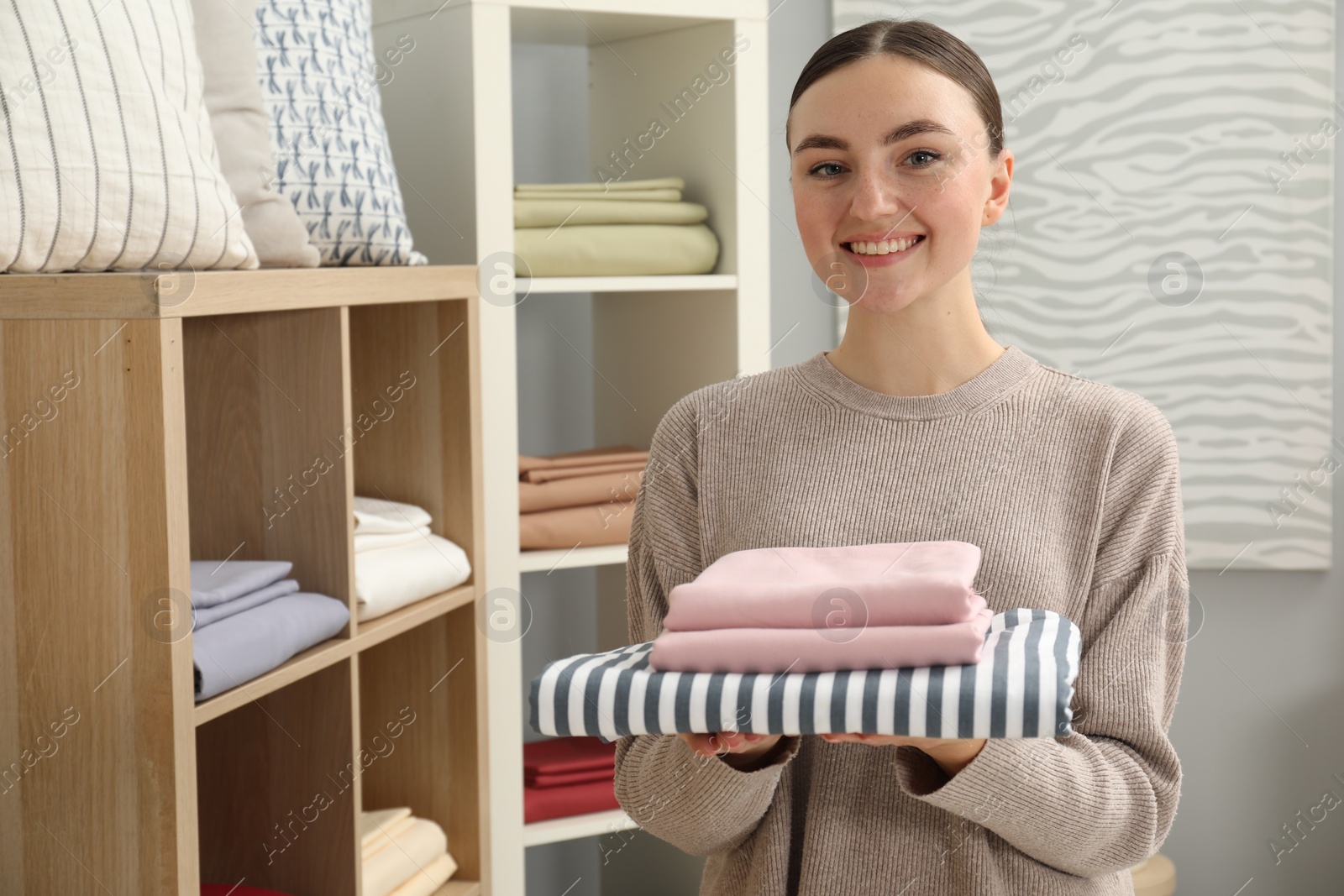 Photo of Smiling young woman with stack of bed linens in shop. Space for text