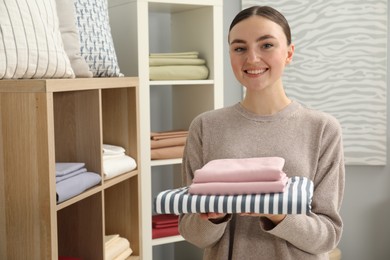 Smiling young woman with stack of bed linens in shop. Space for text