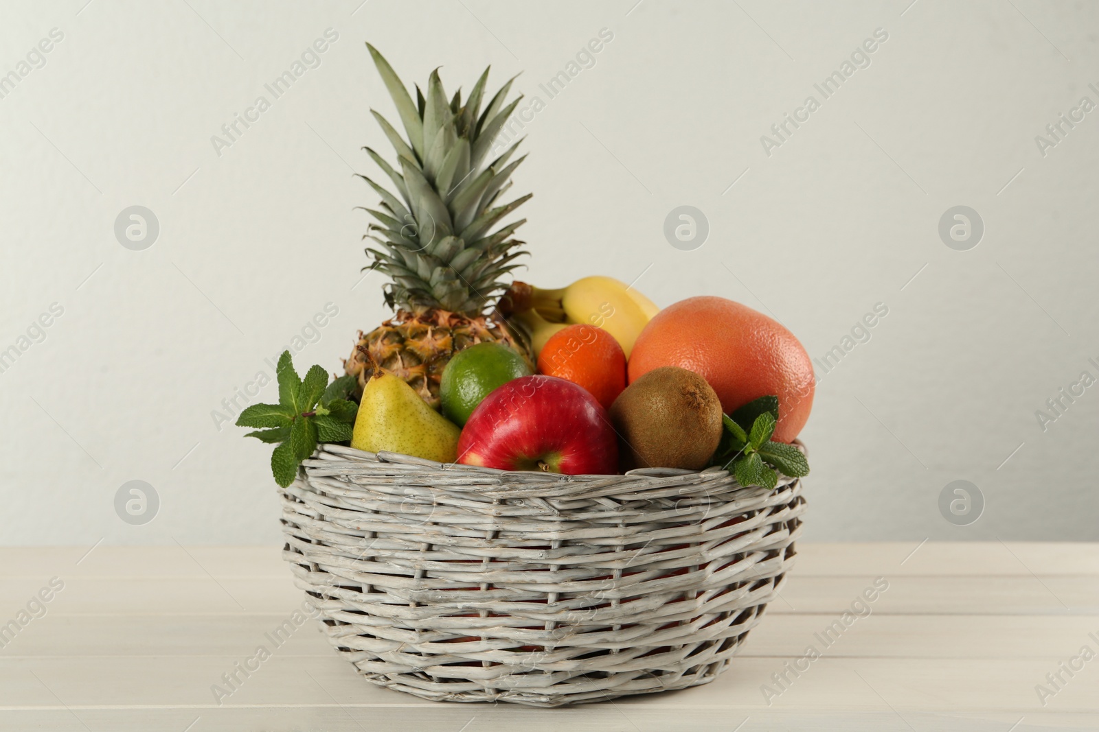 Photo of Fresh ripe fruits in wicker bowl on white wooden table