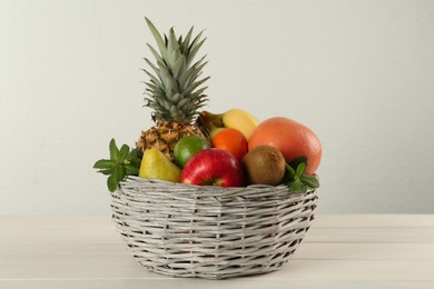Photo of Fresh ripe fruits in wicker bowl on white wooden table