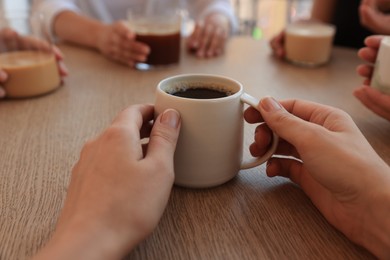 Photo of Woman holding cup of coffee spending time with friends in cafe, closeup