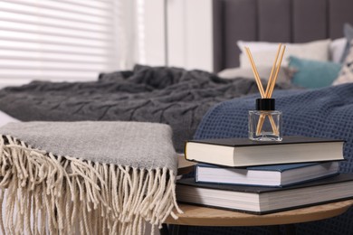 Aromatic reed air freshener, books and plaid on table, space for text