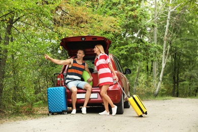 Happy couple near car trunk with suitcases outdoors. Space for text