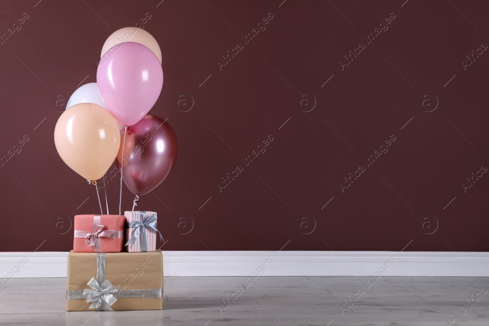 Photo of Many gift boxes and balloons near brown wall. Space for text
