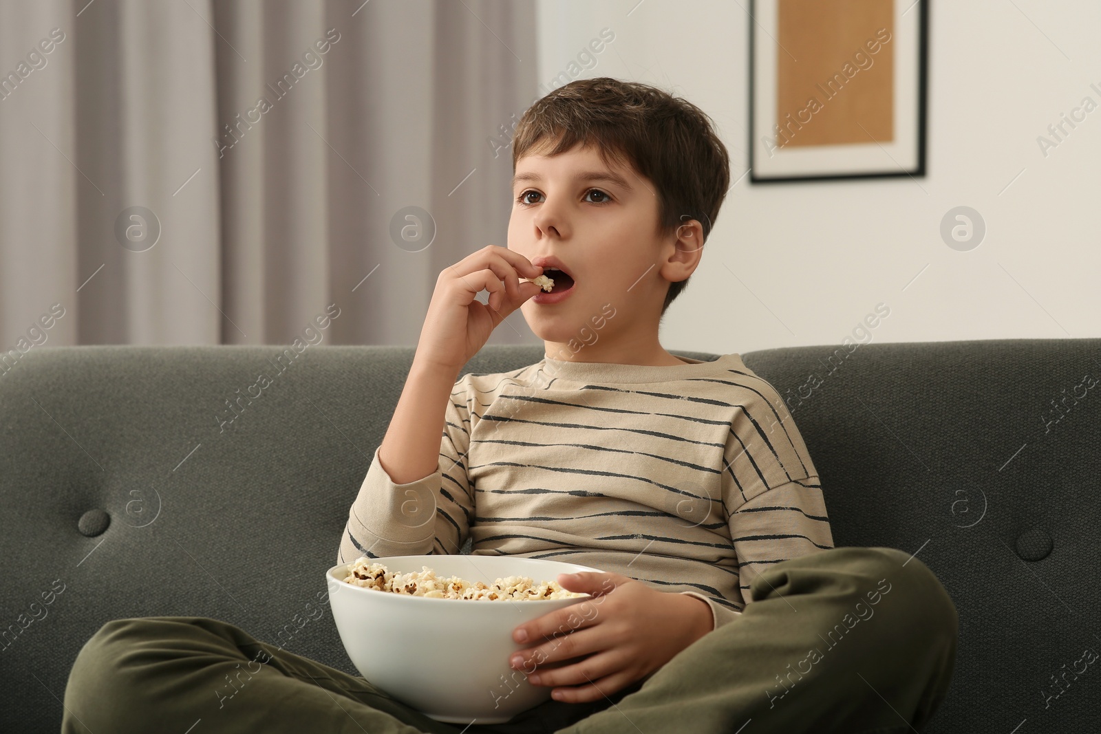 Photo of Little boy eating popcorn while watching TV at home