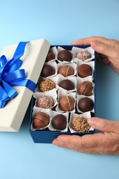 Photo of Woman with box of delicious chocolate candies on light blue background, closeup