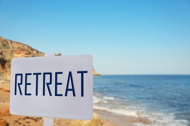 Wooden sign with word Retreat and picturesque view of beautiful beach