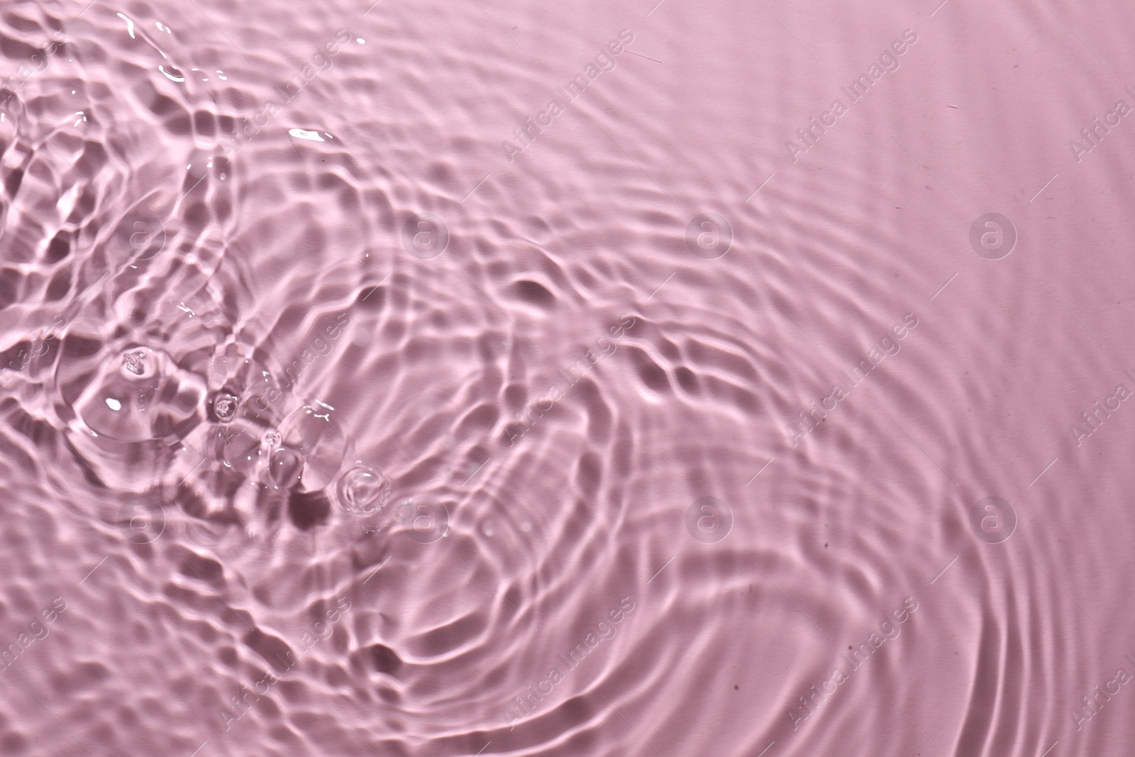 Photo of Rippled surface of clear water on pink background, top view