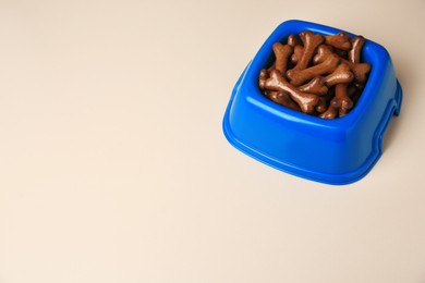 Photo of Blue bowl with bone shaped dog cookies on light background, space for text