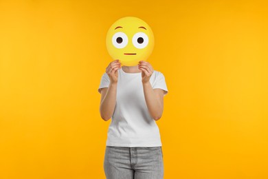 Woman covering face with surprised emoticon on yellow background