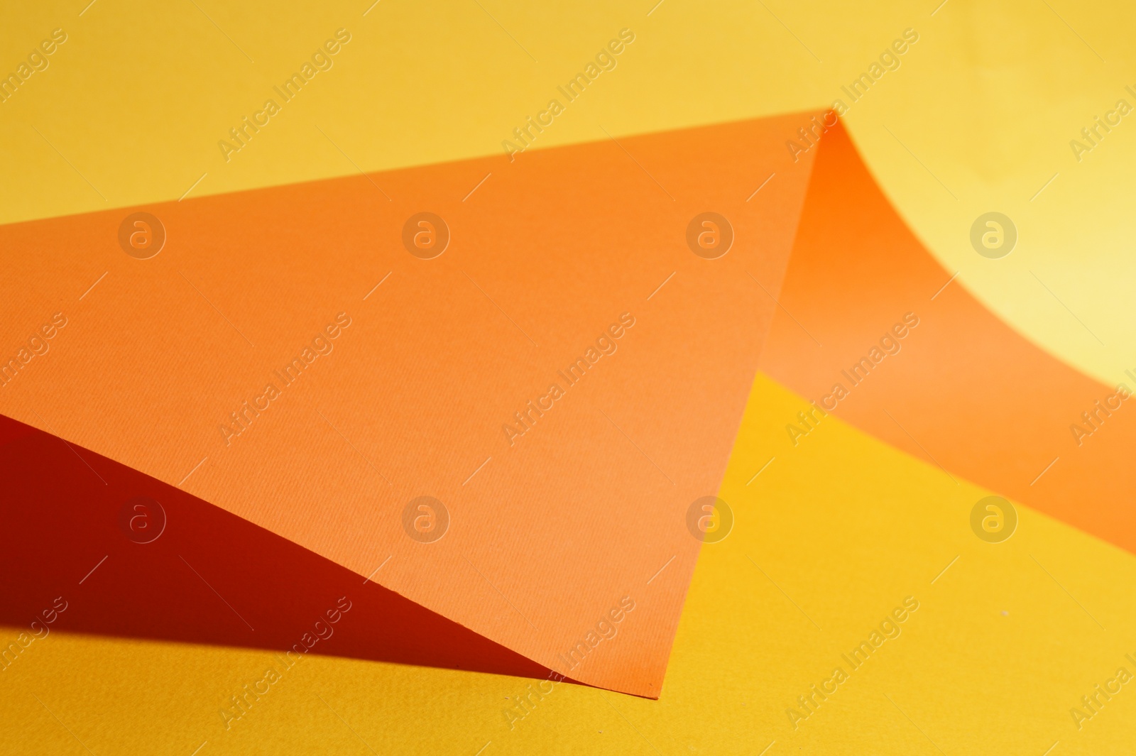 Photo of Orange paper sheet on yellow background, closeup