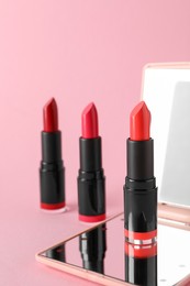 Photo of Different beautiful lipsticks and mirror on pink background