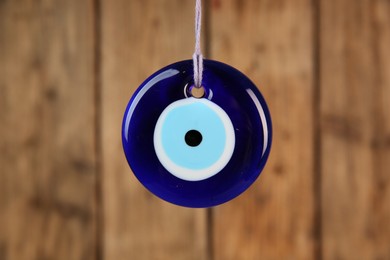 Photo of Evil eye amulet hanging near wooden wall, closeup