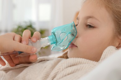 Photo of Little girl using nebulizer for inhalation in bedroom, closeup