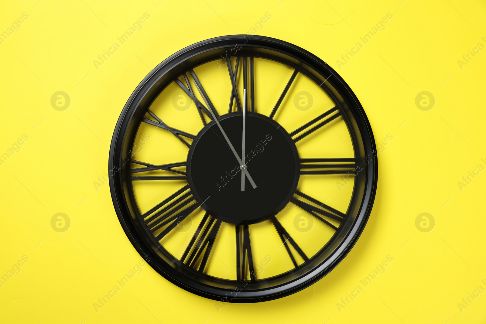 Photo of Clock showing five minutes until midnight on yellow background. New Year countdown