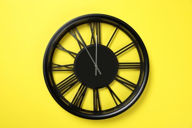 Photo of Clock showing five minutes until midnight on yellow background. New Year countdown