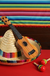 Photo of Mexican sombrero hat, ukulele and maracas on red table
