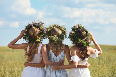 Photo of Young women wearing wreaths made of beautiful flowers in field on sunny day, back view