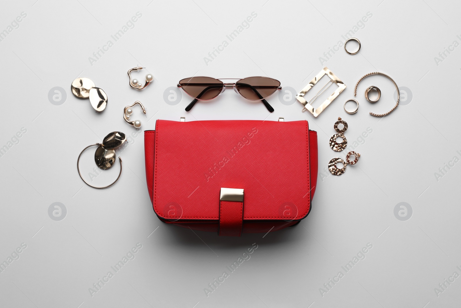 Photo of Stylish woman's bag, sunglasses and bijouterie on light background, flat lay