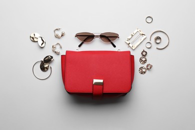 Stylish woman's bag, sunglasses and bijouterie on light background, flat lay