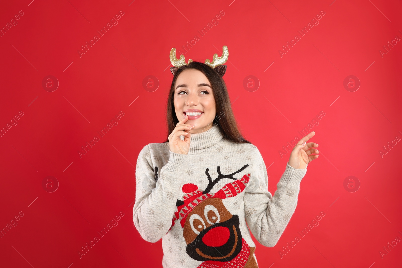 Photo of Young woman in Christmas sweater and deer headband on red background